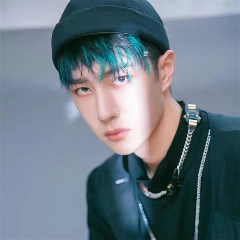 Person with teal hair wearing a black cap and black outfit with chains.