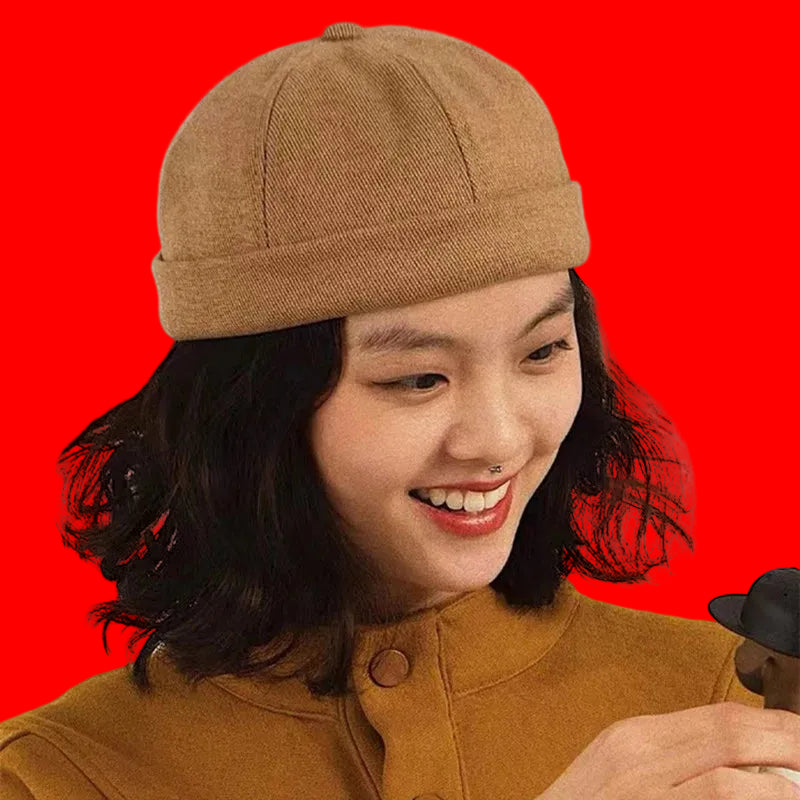 Person wearing a brown cap and smiling, holding a small black hat.